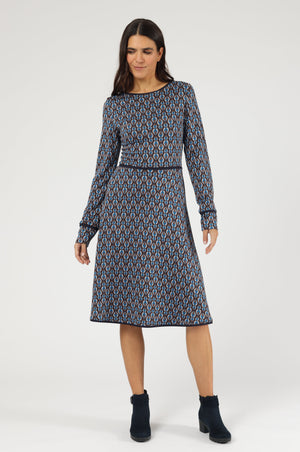 Knielanges Langarm-Kleid mit Rundhalsausschnitt und geometrischem Muster, akzentuiert durch eine dunkelblaue Paspelierung an der Taille.