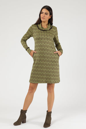 Knieumspielendes Langarm-Kleid mit geometrischem Muster in Gold- und Brauntönen. Besondere Details sind der weite, umschlagbare Kragen sowie die dunkel paspelierten Eingrifftaschen und Ärmelbündchen