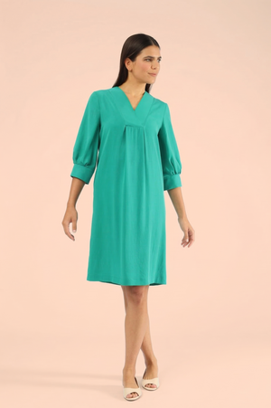 Model in einem knielangen, locker sitzenden, smaragdgrünen Tunikakleid mit V-Ausschnitt, Dreiviertel-Puffärmeln und gerafftem Mieder
