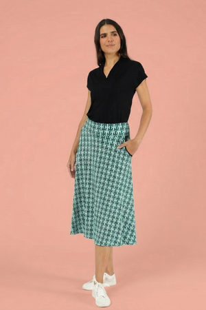 Mittellanger A-Linien-Rock für Damen mit einzigartigem teal-grünem geometrischem Druck, kombiniert mit schwarzem Kurzarm-Top und weißen Turnschuhen.