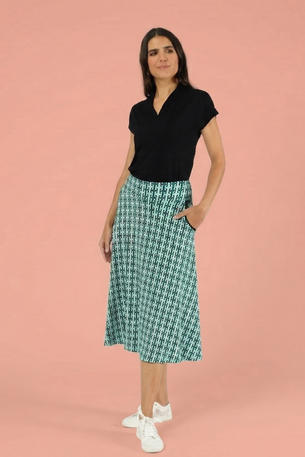 Mittellanger A-Linien-Rock für Damen mit einzigartigem teal-grünem geometrischem Druck, kombiniert mit schwarzem Kurzarm-Top und weißen Turnschuhen.