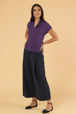 Elegantes Damen-Outfit bestehend aus einer violetten Kurzarm-Bluse mit geometrischem Muster und einer dunkelblauen, weiten Culotte-Hose